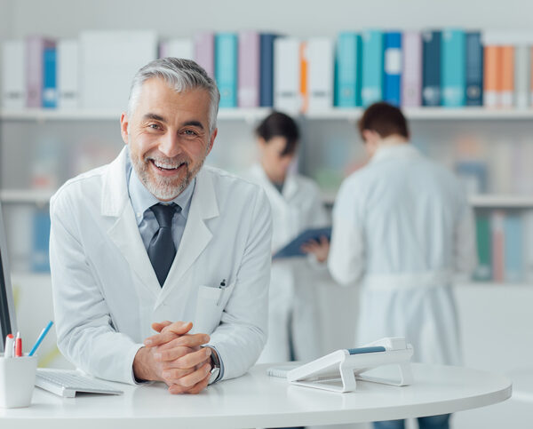 Smiling confident doctor at the reception desk, medical staff working on the background